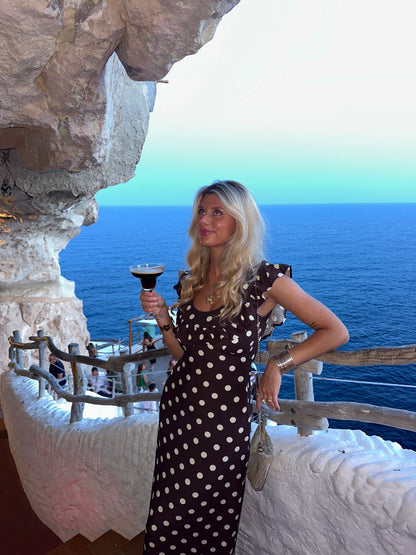 Brown polka dot maxi dress with ruffle sleeves at coastal location with ocean view