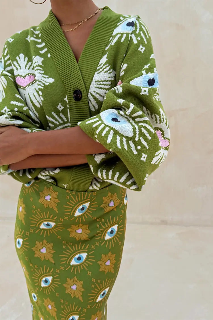 Close-up of green knit cardigan showing white eyelash pattern with blue eye and pink heart embroidery