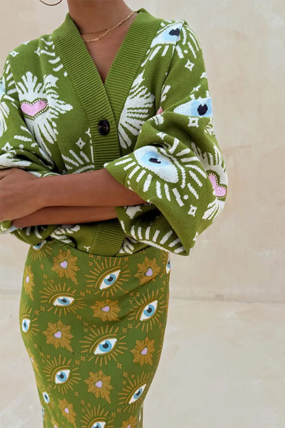Close-up of green knit cardigan showing white eyelash pattern with blue eye and pink heart embroidery