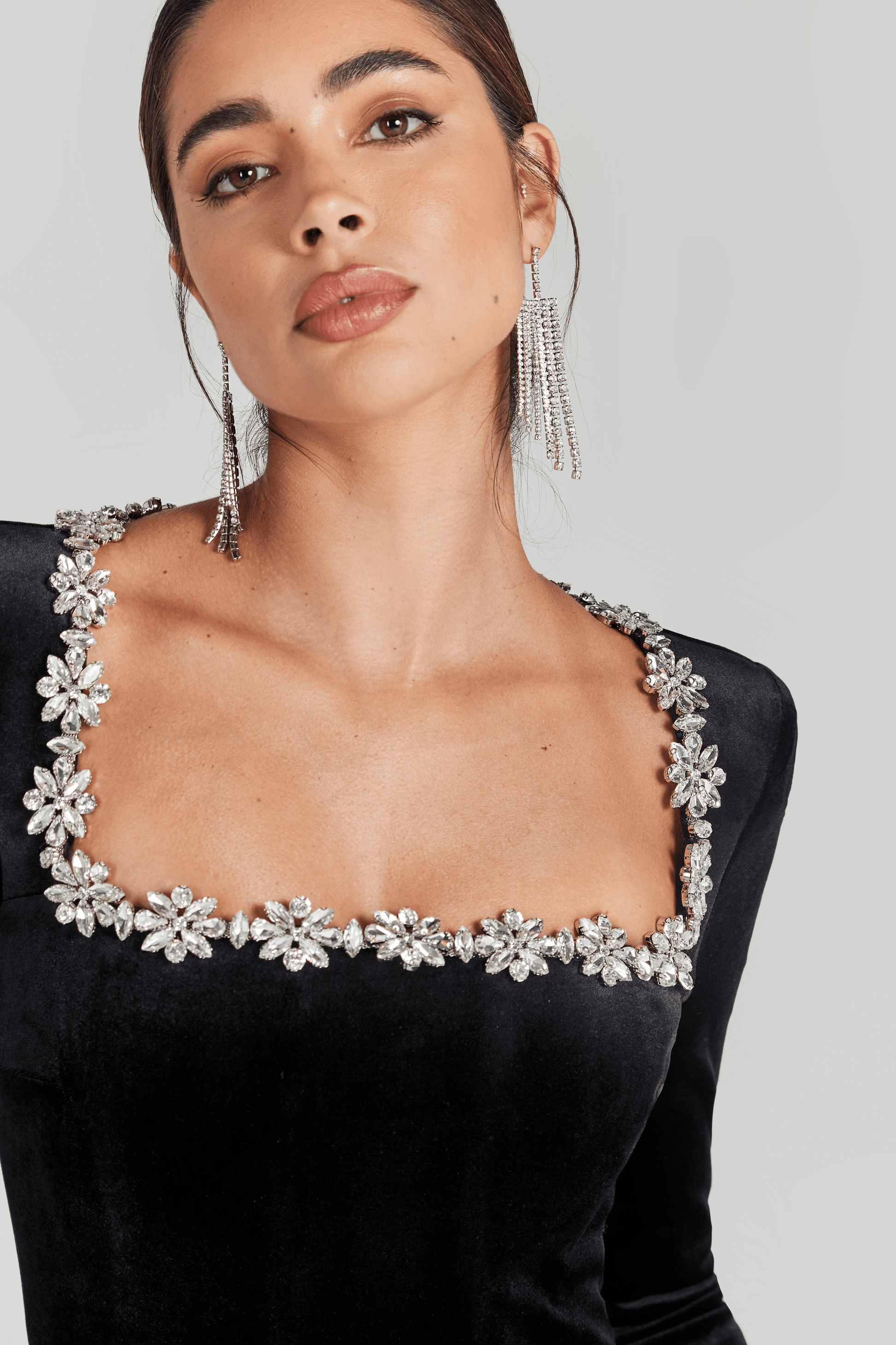 Detail view of crystal flower embellishments along square neckline of black velvet jumpsuit