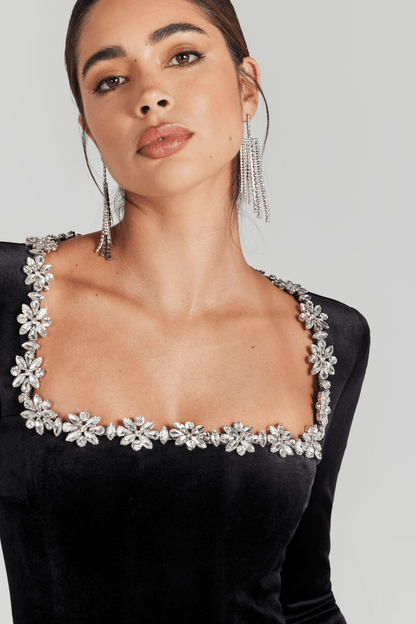 Detail view of crystal flower embellishments along square neckline of black velvet jumpsuit