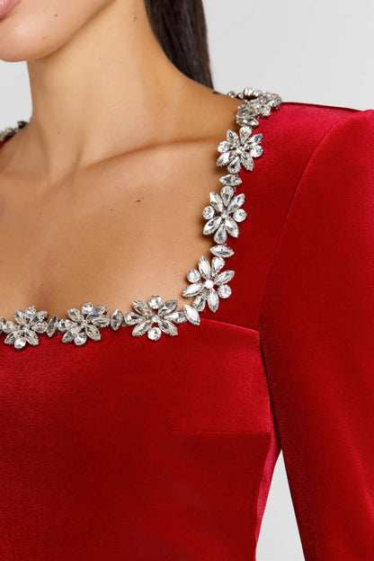 Close-up of red velvet jumpsuit showing crystal flower trim on square neckline and shoulder