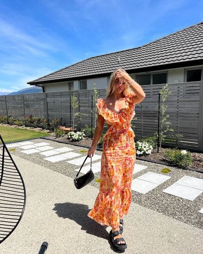 Woman wearing coral floral ruffle maxi dress styled with sandals for summer occasions