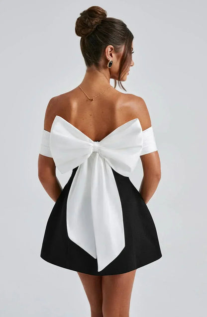 Back view of black mini dress with large white bow detail and off-shoulder sleeves