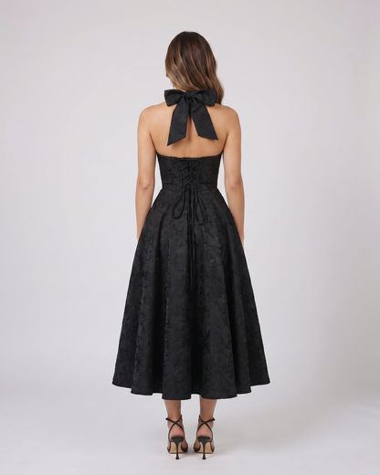 Back view of black floral jacquard halter midi dress showing lace-up corset back with halter tie-back forming a bow