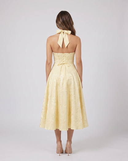 Back view of yellow floral jacquard halter midi dress showing lace-up corset back with halter tie-back forming a bow