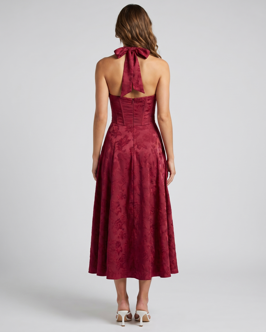 Back view of red floral jacquard halter midi dress showing lace-up corset back with halter tie-back forming a bow