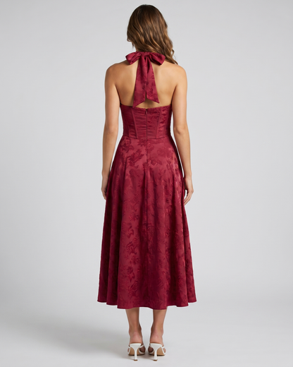 Back view of red floral jacquard halter midi dress showing lace-up corset back with halter tie-back forming a bow