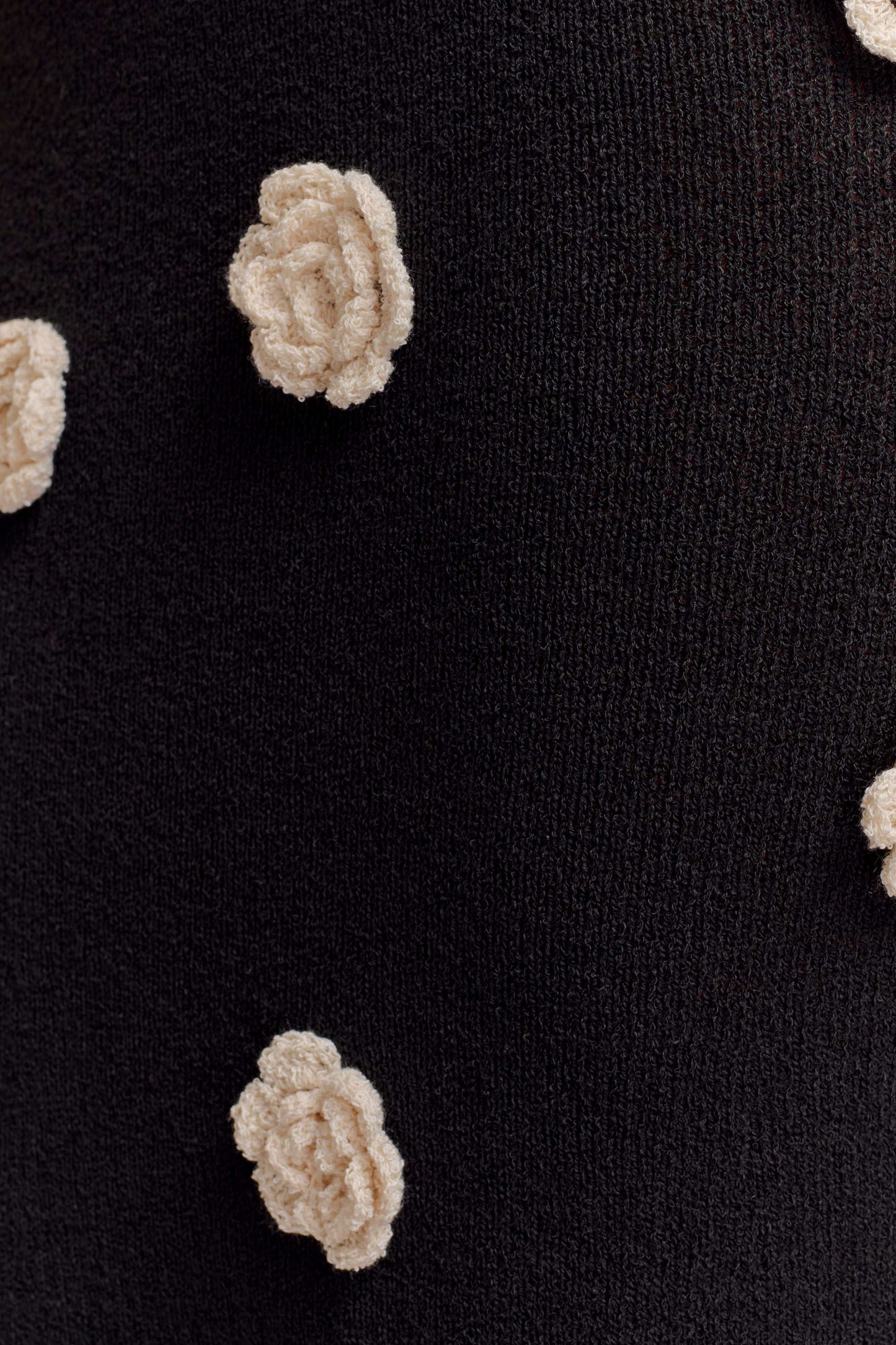 Close-up of cream textured rose appliqués on black knit fabric