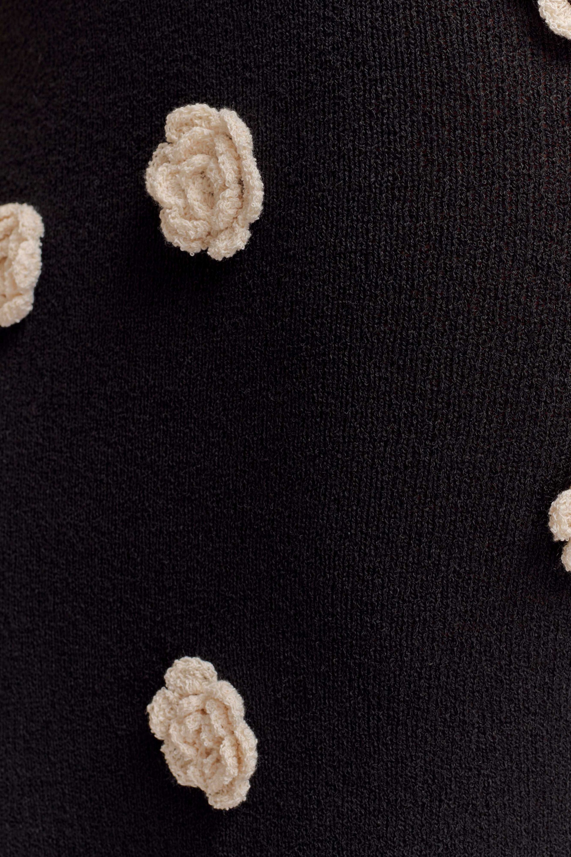 Close-up of cream textured rose appliqués on black knit fabric